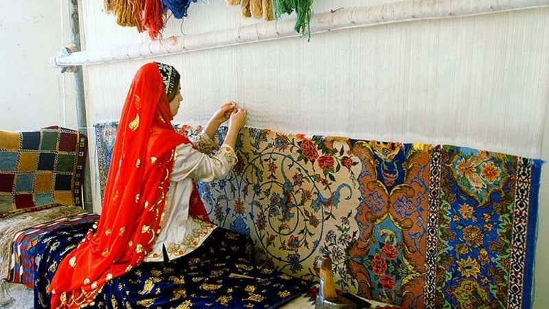 An Iranian village girl in traditional local dress, weaving a carpet